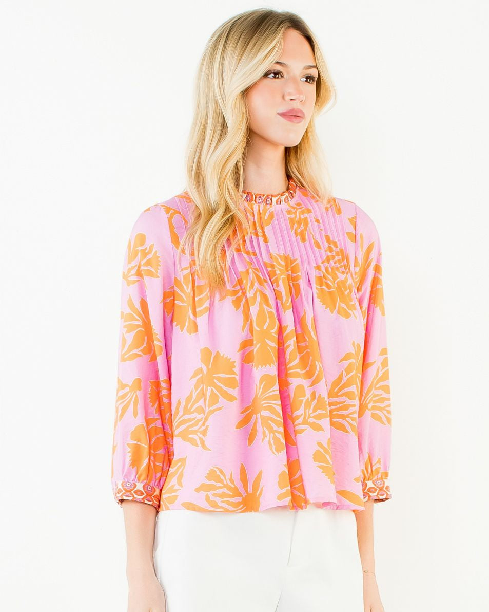 Woman wearing a pink and orange floral blouse with a white skirt on a white background