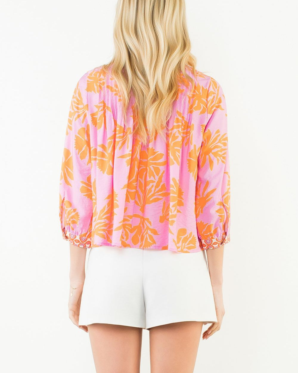 Woman wearing a pink and orange floral blouse with white shorts on a white background