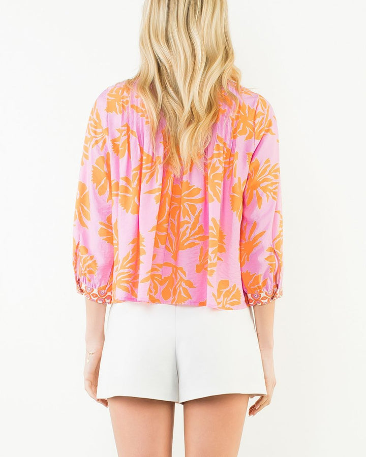 Woman wearing a pink and orange floral blouse with white shorts on a white background