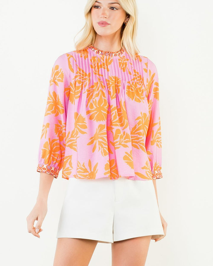 Woman wearing a pink and orange floral blouse with white shorts on a white background