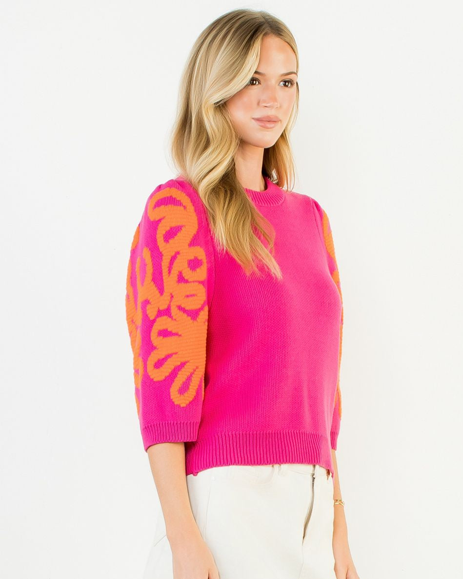 Woman wearing a bright pink sweater with orange butterfly designs on sleeves against a white background