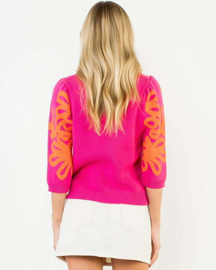 Person wearing a bright pink sweater with orange floral patterns on a white background
