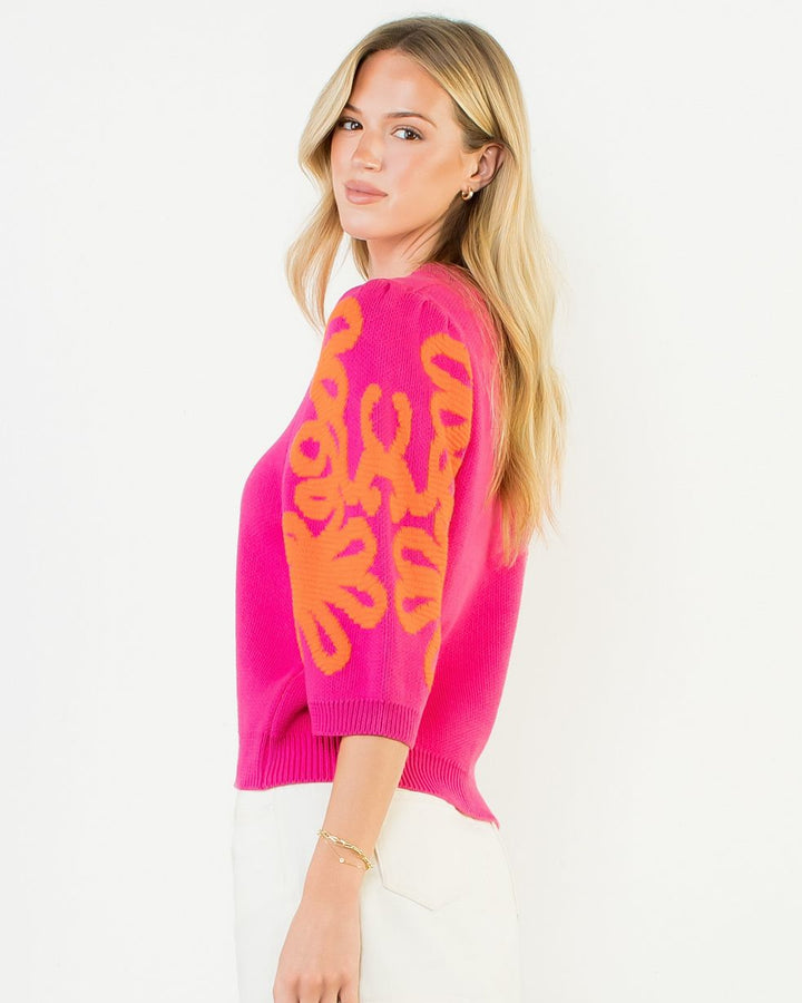 Woman wearing a bright pink sweater with orange patterns on a white background