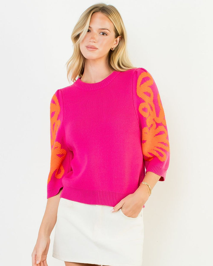 Woman wearing a bright pink sweater with orange patterns on a white background