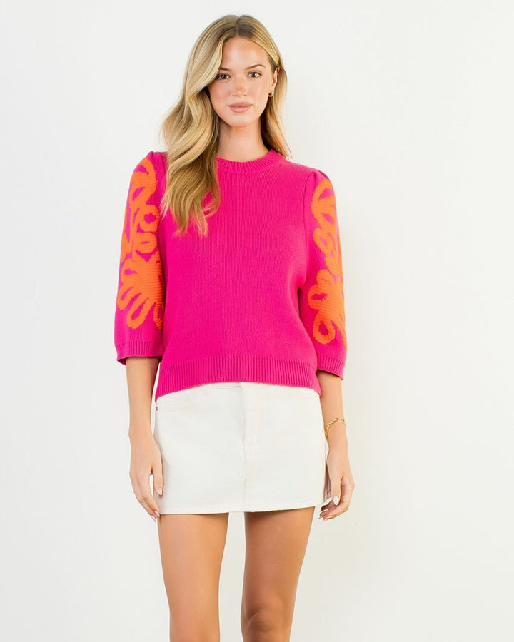 Woman wearing a bright pink sweater with orange sleeves against a white background