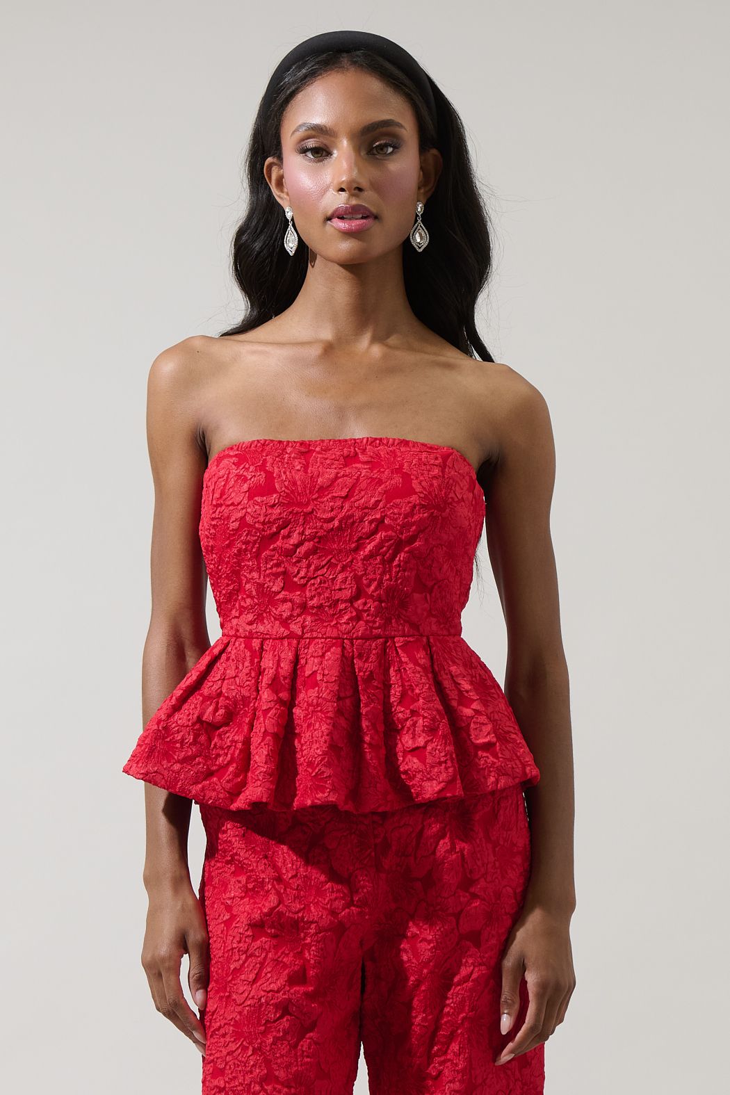 Woman wearing a red strapless peplum top and pants against a plain background