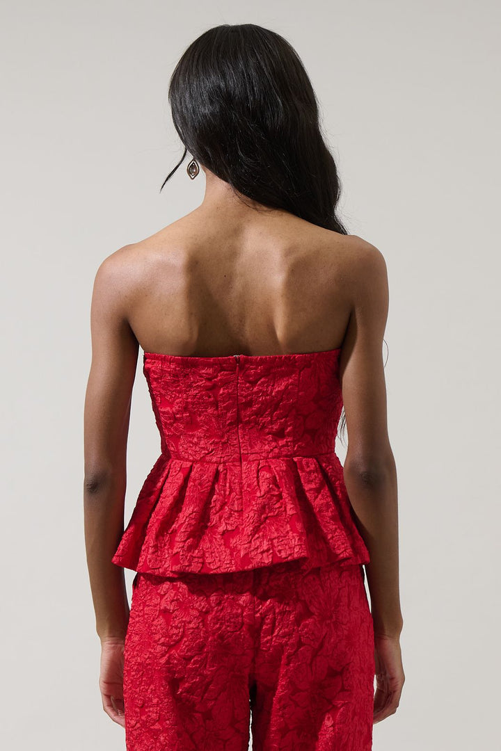 Woman wearing a red strapless peplum top and pants against a plain background