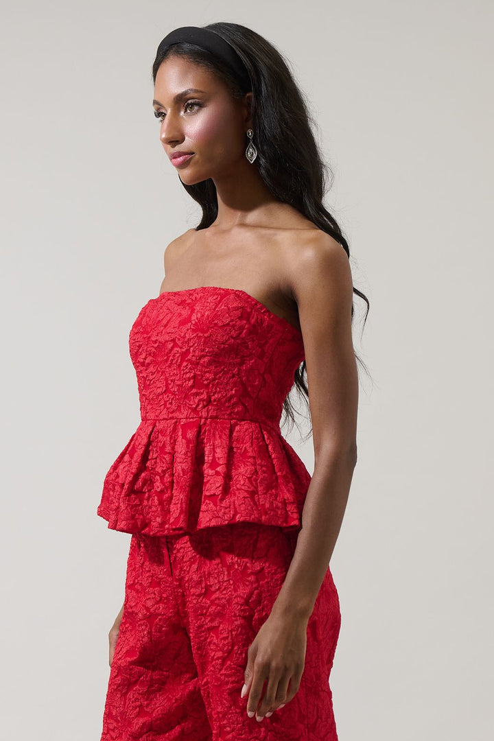 Woman wearing a red strapless peplum top and pants against a plain background