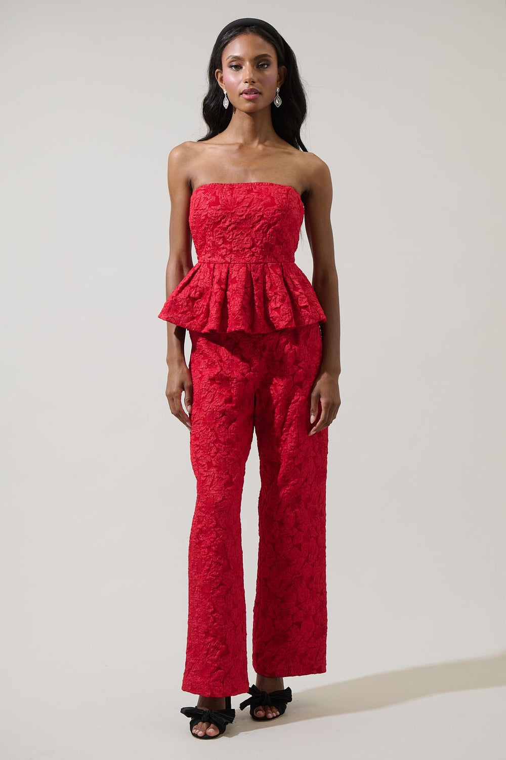 Woman wearing a red strapless peplum top and matching pants on a plain background