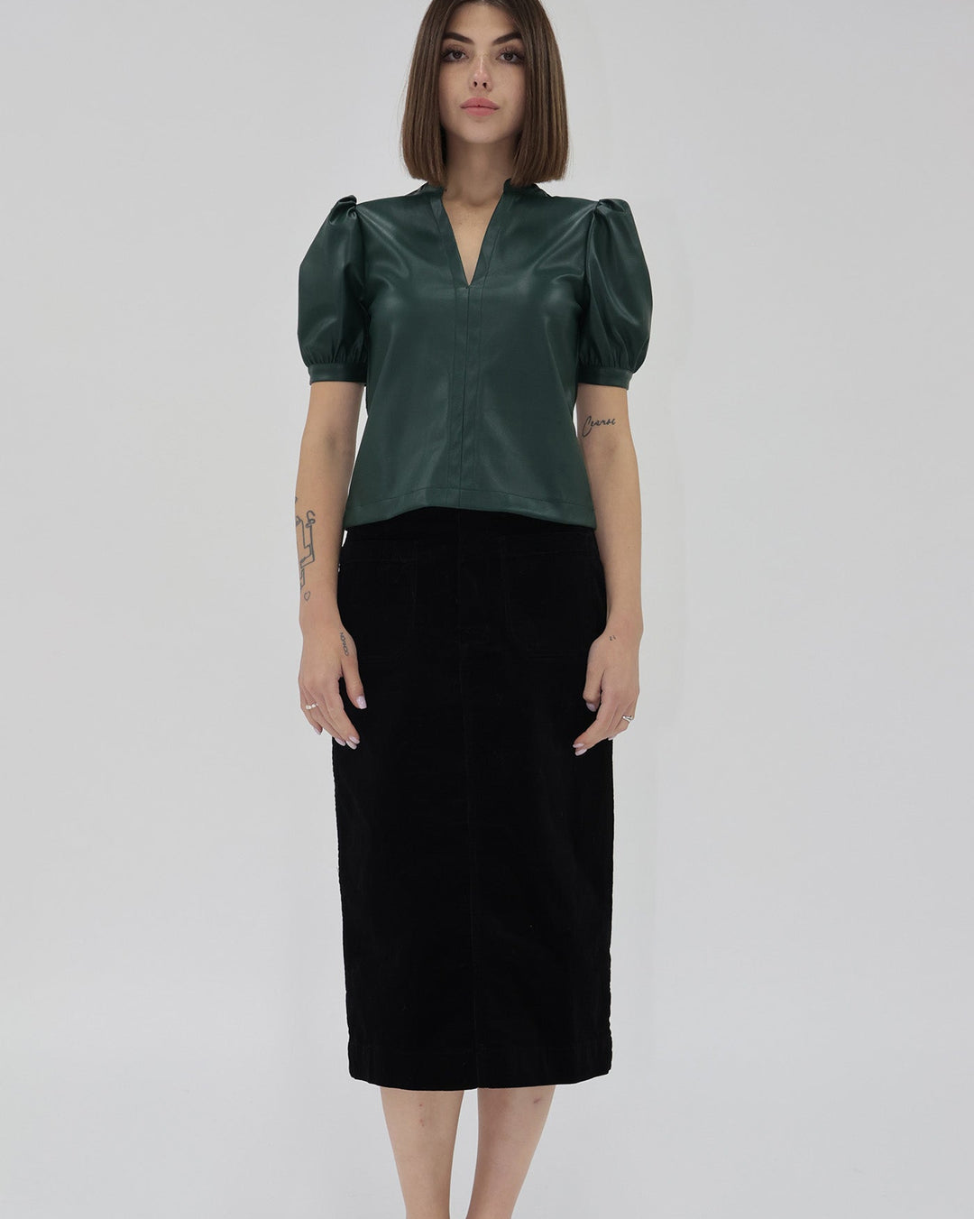 Woman wearing a green blouse with puffed sleeves and a black skirt on a white background