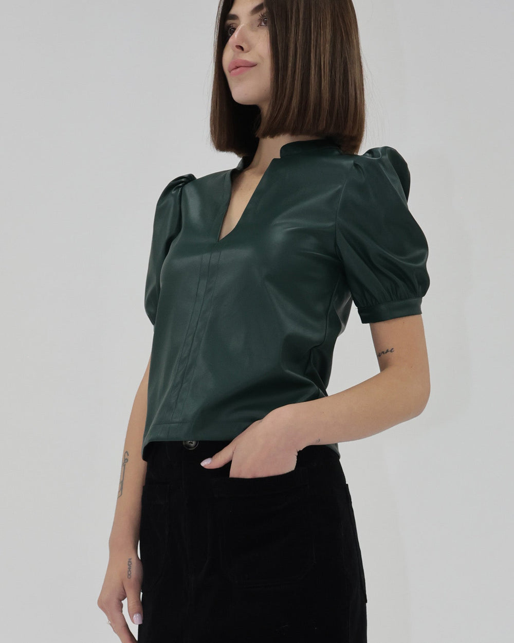 Woman wearing a green blouse with puffed sleeves against a plain background