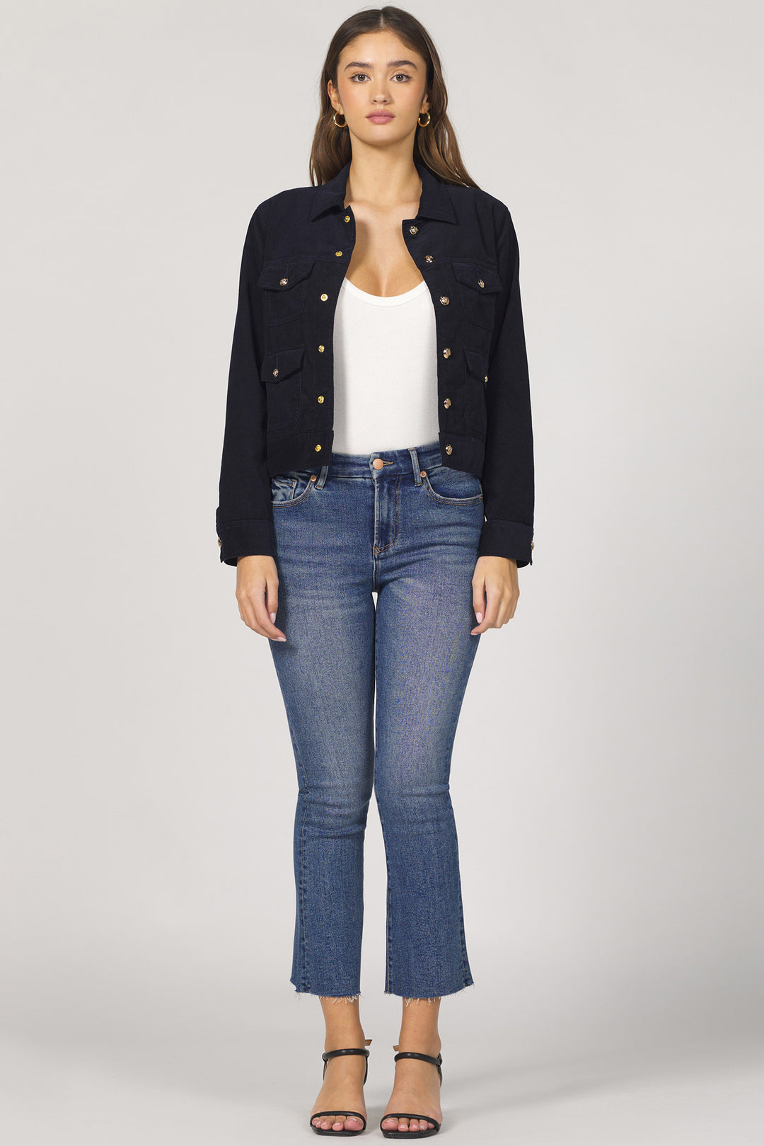Woman wearing a black denim jacket, white top, and blue jeans on a gray background
