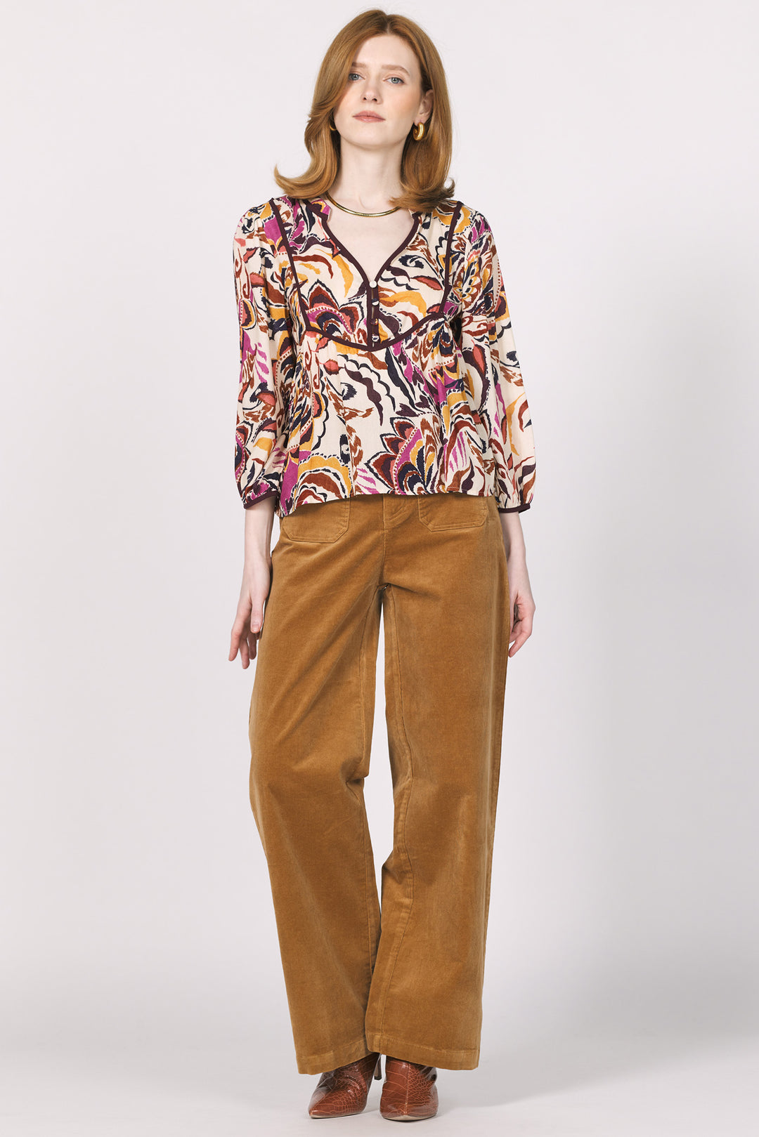 Woman wearing a patterned top and brown pants on a white background