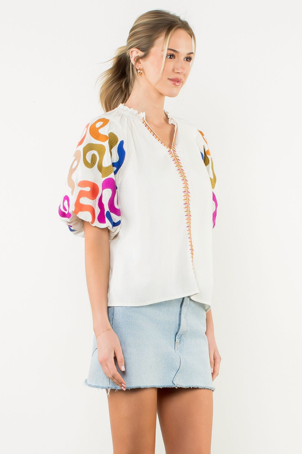 Woman wearing a white blouse with colorful embroidery and a light blue skirt on a white background