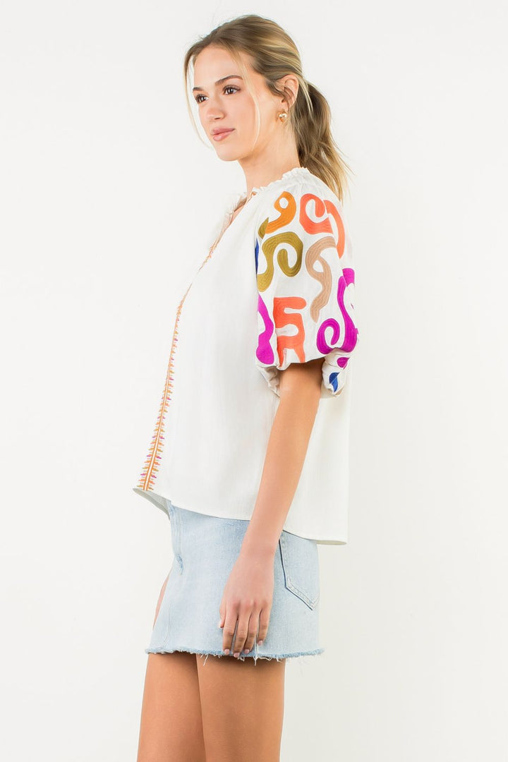 Woman wearing a white blouse with colorful patterns and a light blue skirt on a white background