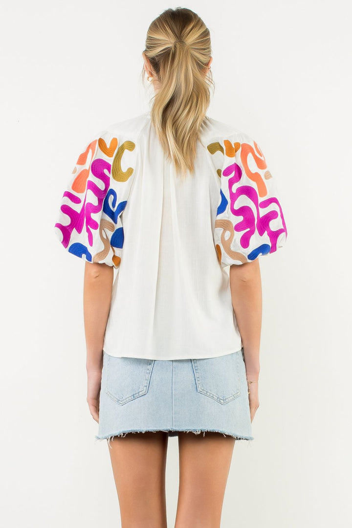 Person wearing a white blouse with colorful abstract patterns on sleeves against a white background