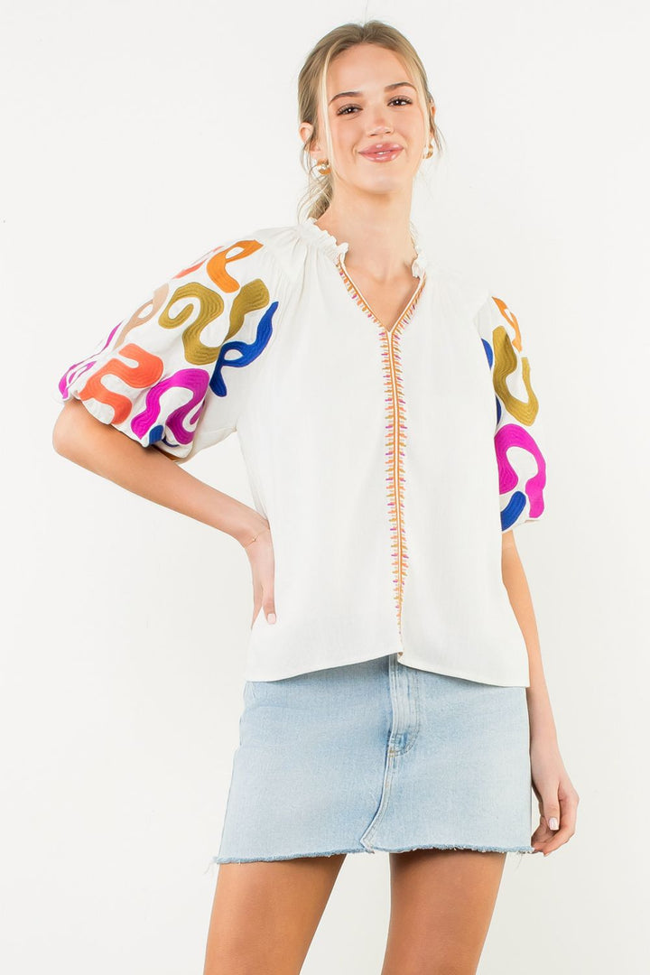 Woman wearing a white blouse with colorful sleeves and a light blue denim skirt on a white background