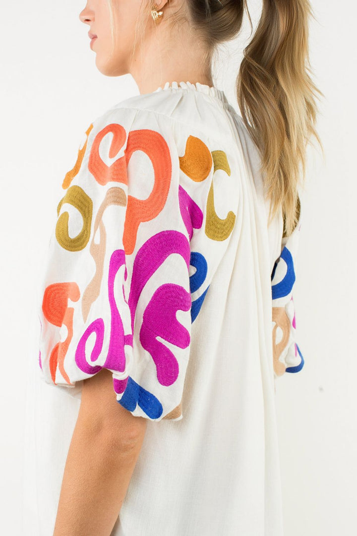 Person wearing a white top with colorful abstract patterns on sleeves against a white background