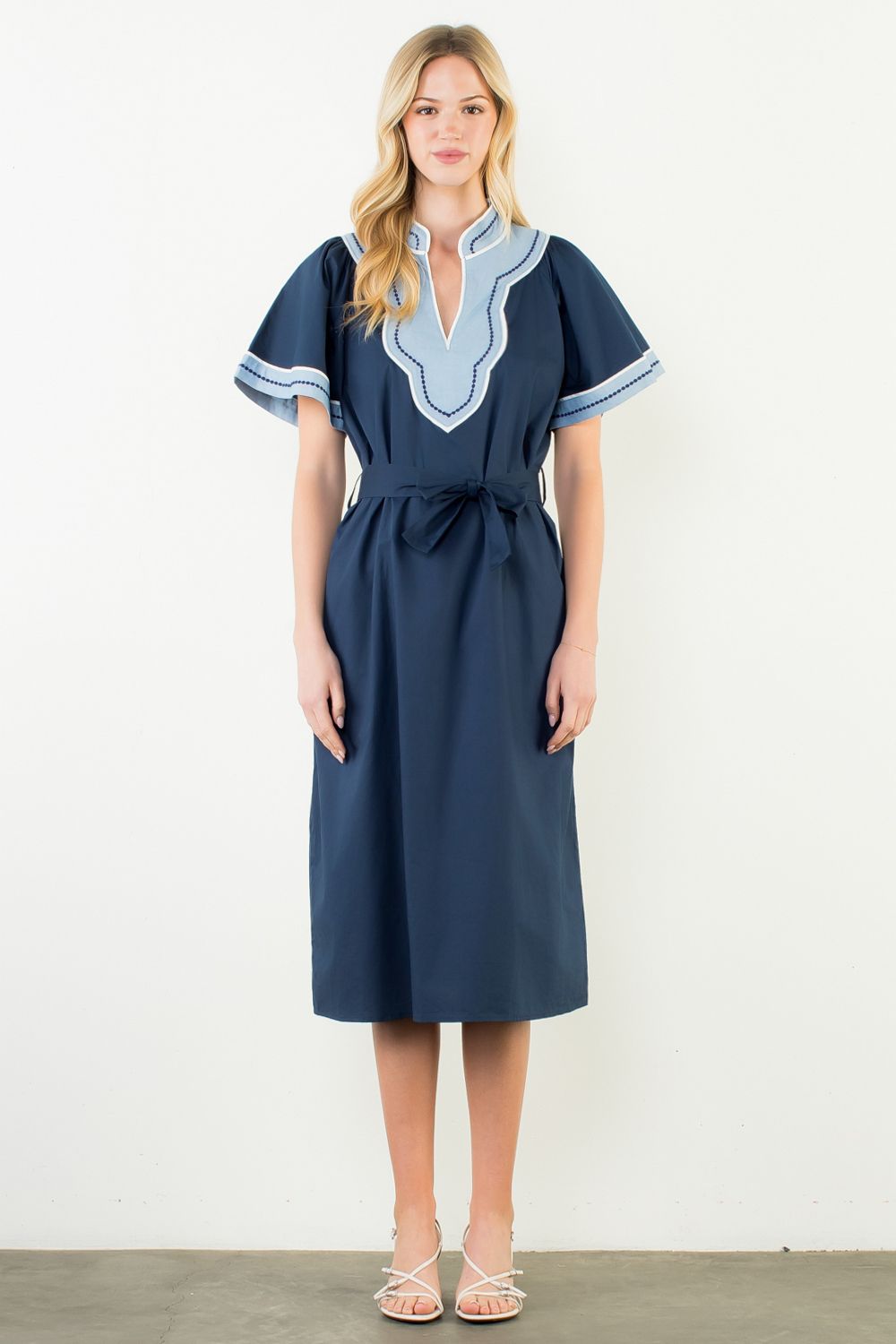 Woman wearing a navy dress with light blue embroidery on a white background