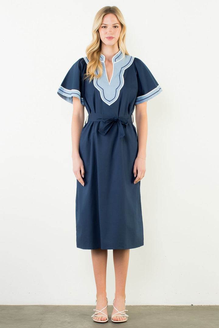 Woman wearing a navy dress with light blue embroidery on a white background