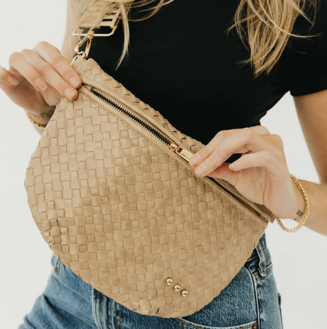 Person holding a woven beige bag with a plain background