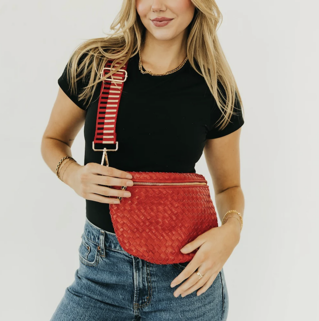 Woman holding a red textured bag with a striped strap against a plain background