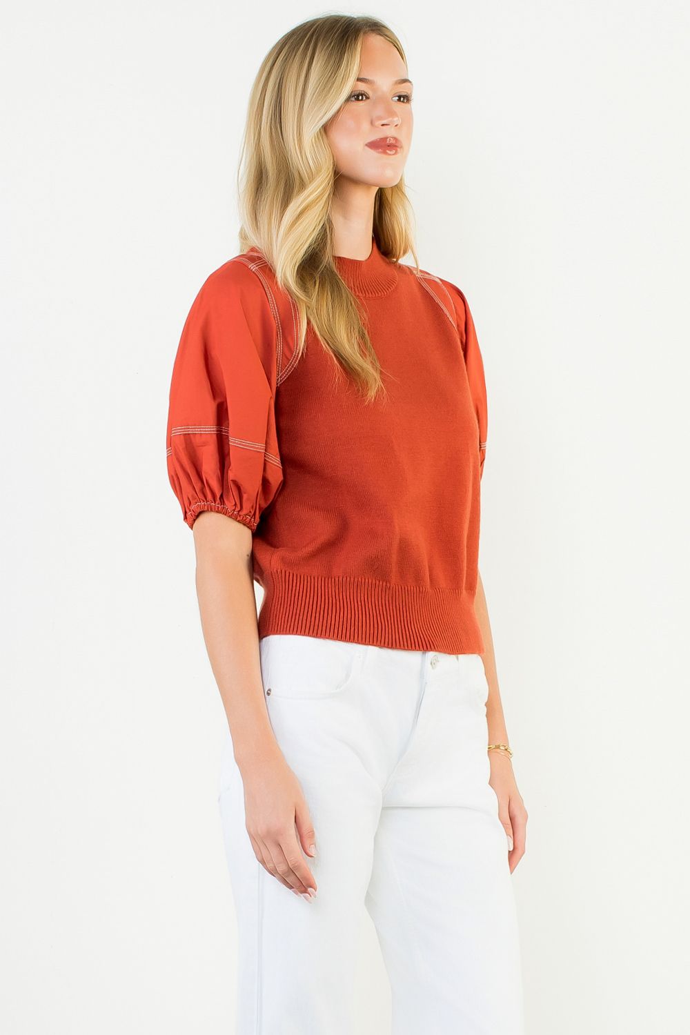 Woman wearing an orange sweater with white pants on a white background