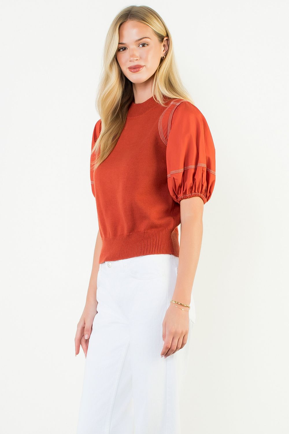 Woman wearing a rust-colored sweater with puff sleeves on a white background