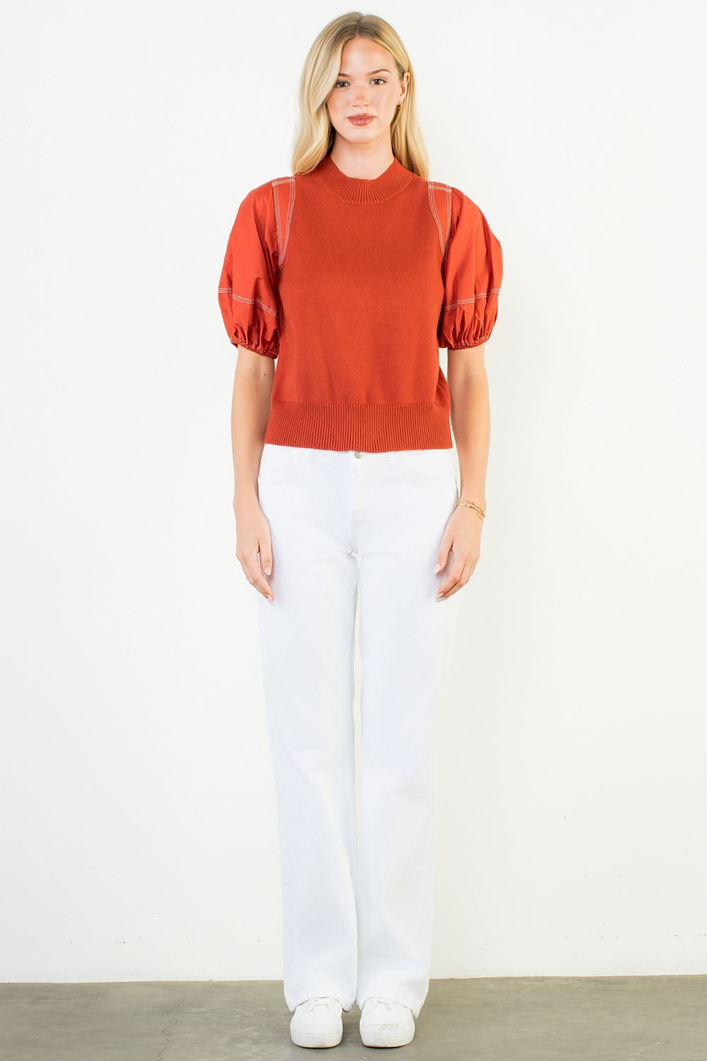 Woman wearing a red blouse and white pants on a plain background