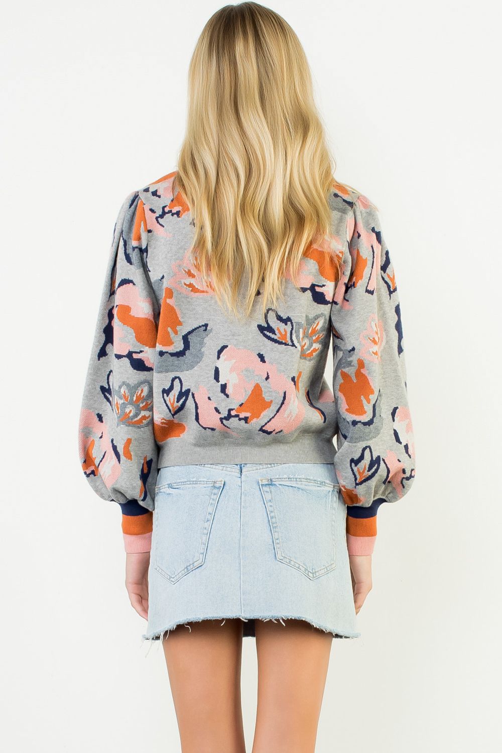 Person wearing a colorful floral sweater and denim skirt on a white background