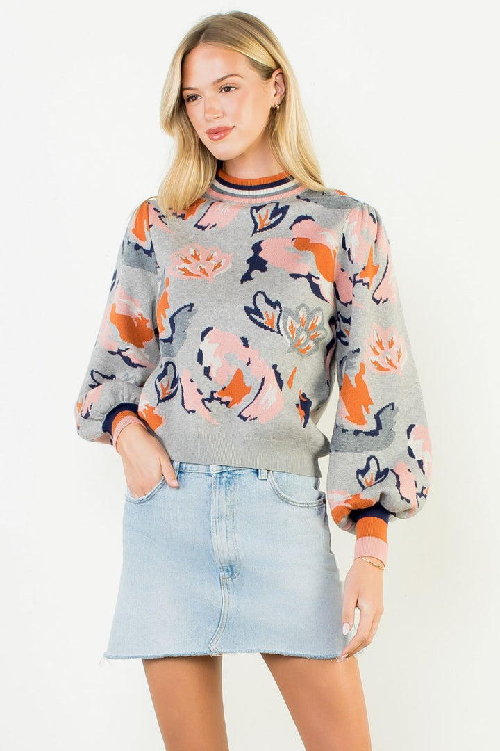 Woman wearing a colorful floral sweater and denim skirt on a white background