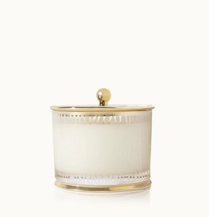 A white candle with a wood grain pattern and a gold lid.