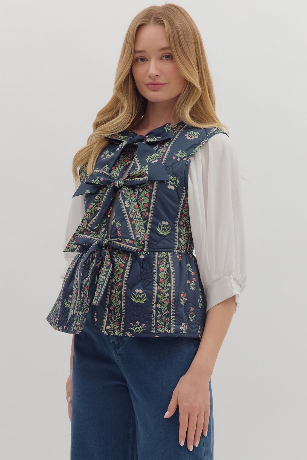 Woman wearing a patterned blue vest over a white shirt with a plain background