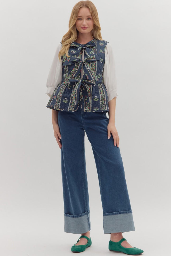 Woman wearing a blue patterned vest over a white shirt with blue jeans on a white background