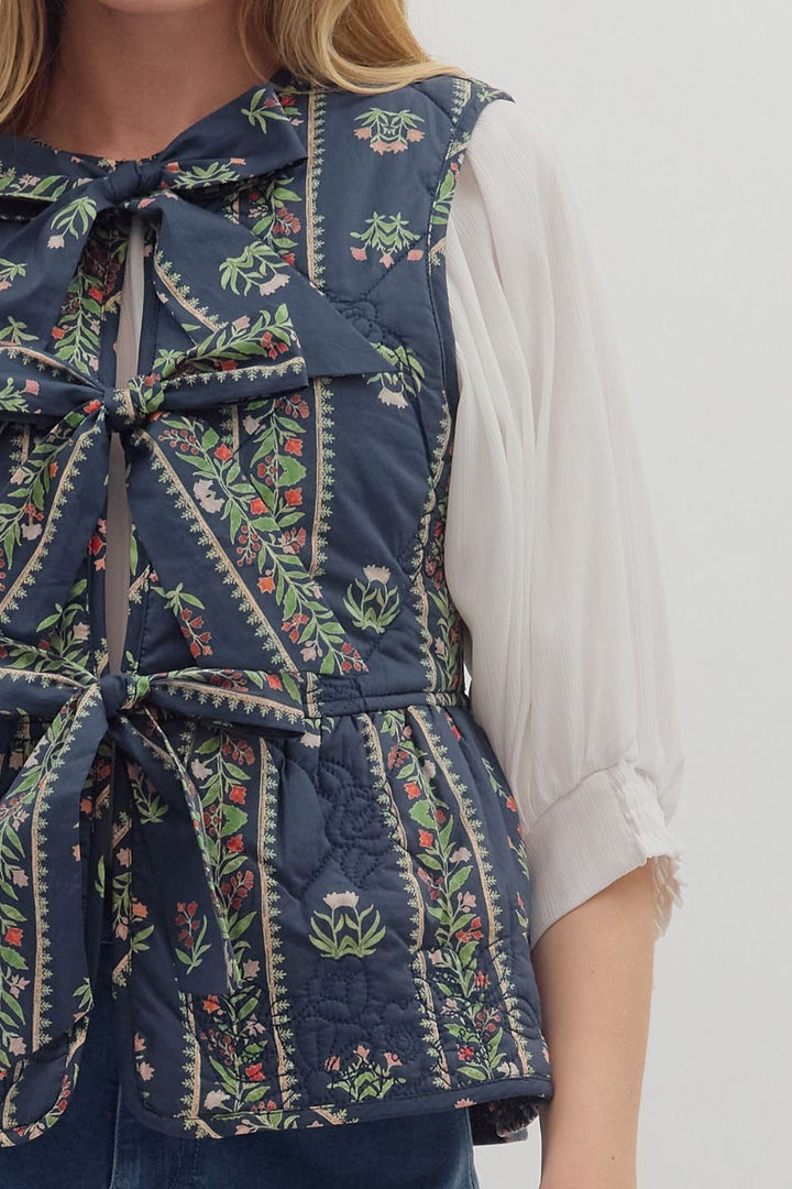 Person wearing a blue floral-patterned vest with a white shirt underneath on a plain background
