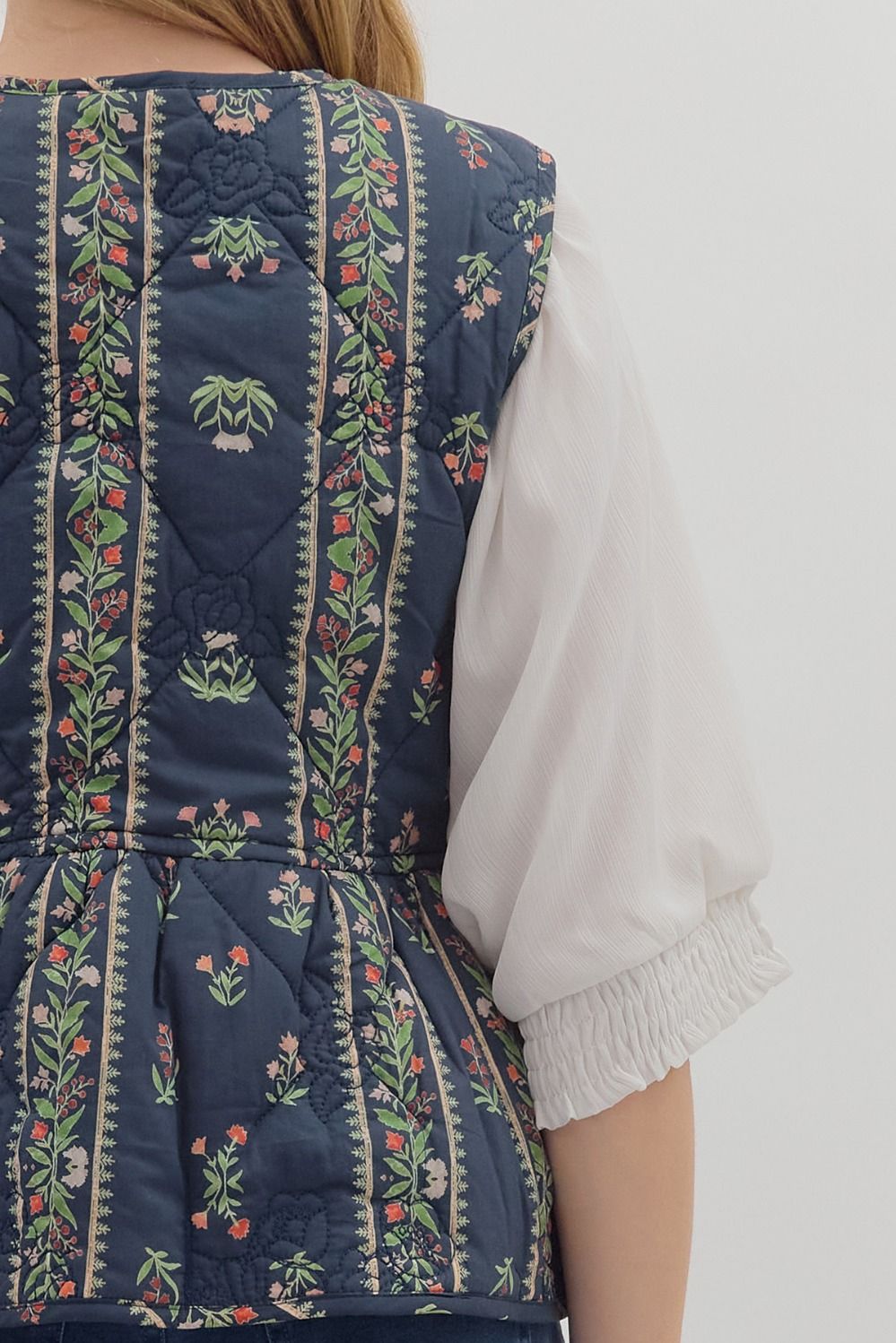 Navy blue embroidered vest over a white blouse on a plain background