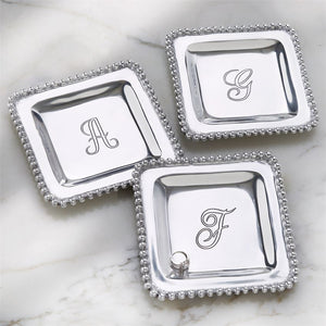 The possibilities are endless! This perfectly giftable trinket tray has multiple uses. Style it as a true bedside or vanity trinket tray, place it in your entryway as your catchall, or use it to entertain as a cocktail napkin holder. This high-polished cast aluminum trinket dish features dimensional beaded edge and engraved center initial. Perfectly giftable in elegant paper wrapped gift box.  Dimensions: 7" x 7"
