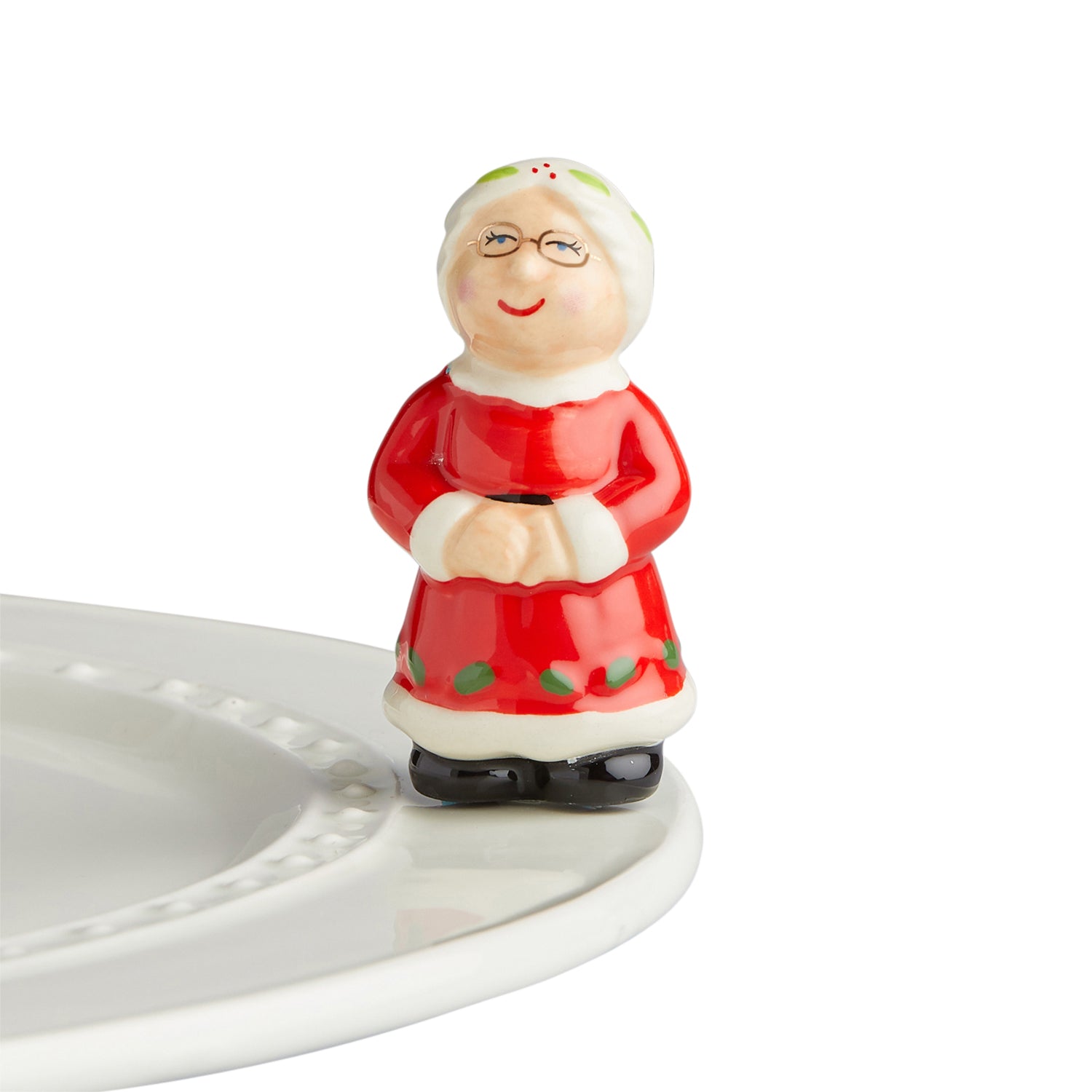 The Nora Fleming Mini Mrs. Claus is here! Mrs. Claus is stepping in to give Santa a helping hand! You’ll love her cute red dress and her wire-rimmed glasses, too! Pair her with Santa for the perfect Christmas setting! 