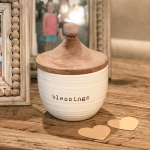 Count your blessings and keep them close with this beautiful jar with debossed sentiment "blessings" stamped into the ceramic covered with a mango wood lid.  Arrives with ten kraft paper heart slips. Size: jar is 6" high and 4 1/2" round. Each heart slip is 2 1/4" x 2 1/2".