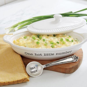 3-piece set. Ceramic au gratin baker features debossed “One hot little number” sentiment, fluted details, side handles, removable lid and arrives tied with vintage-style stamped silverplated spoon.  Ceramic is oven safe to 350 degrees. Size: baker with lid 3″ x 9″ x 5″, spoon is 5 1/2″